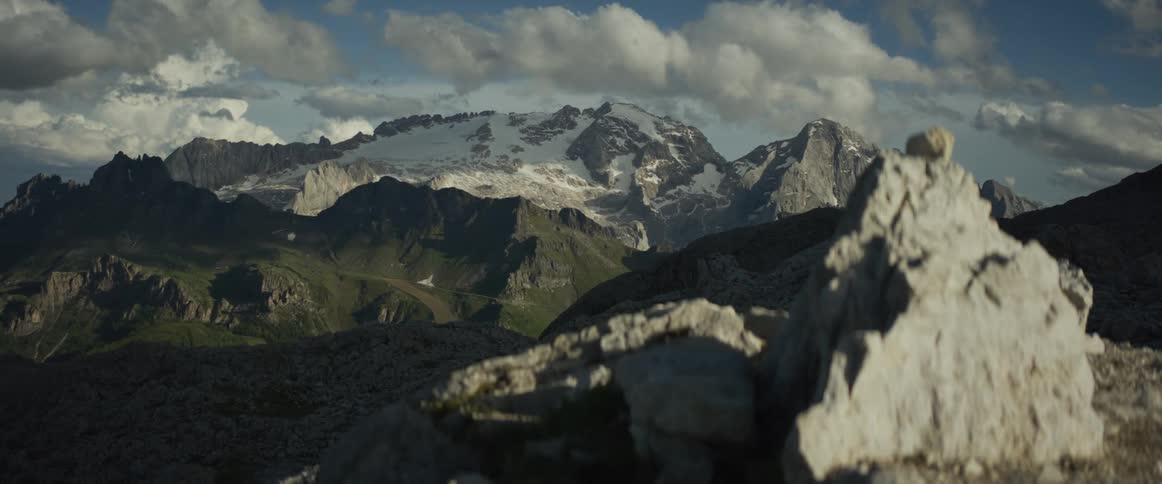 A slow tracking shot reveals a stunning view of a snow-capped mountain range under a partly cloudy sky