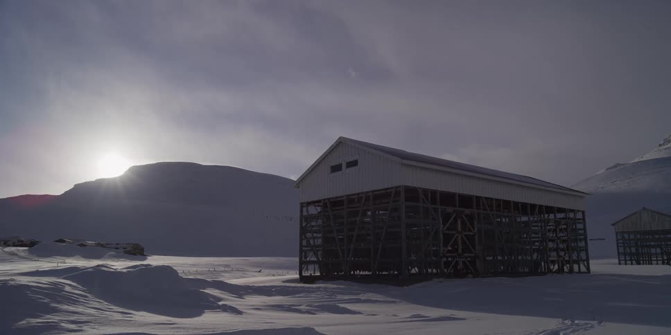 A traditional fish drying rack stands in a vast, snowy landscape as the winter sun hangs low in the sky