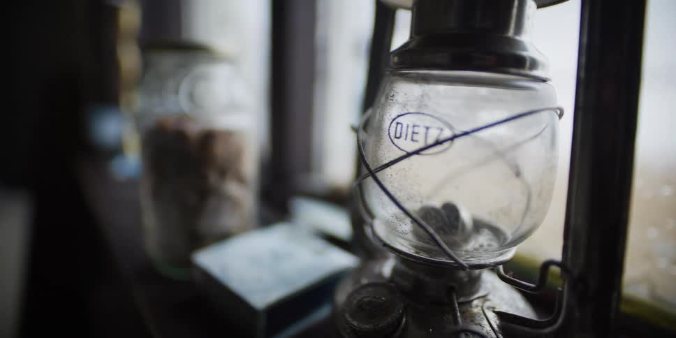 Close up of a weathered Dietz oil lamp resting on a rustic wooden windowsill