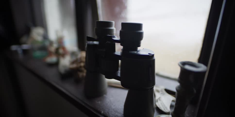 A slow dolly shot of binoculars and a candlestick silhouetted on a dusty windowsill