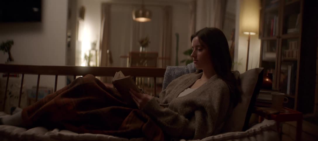 Cozy evening scene of a woman reading a book on the couch, wrapped in a warm blanket in a dimly lit room