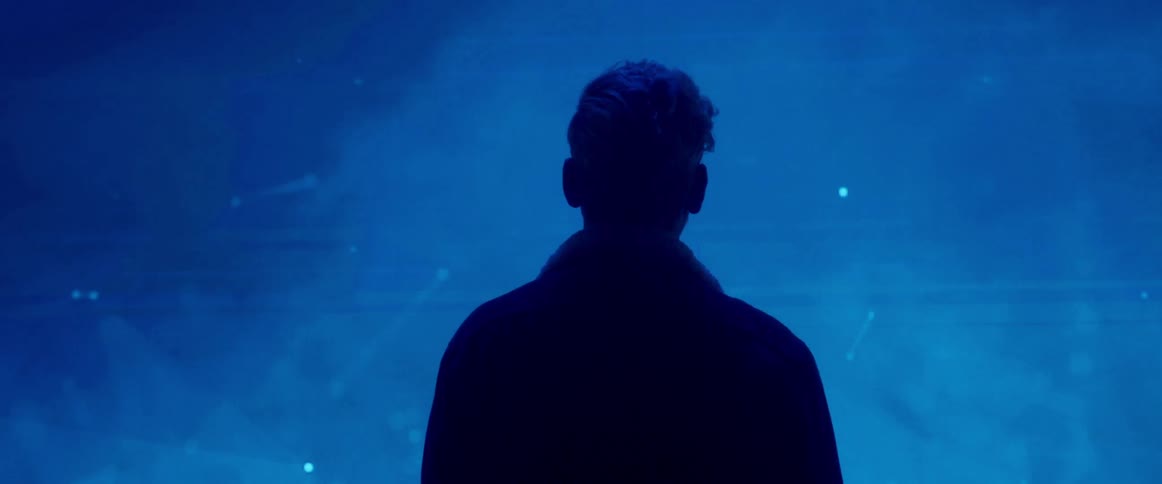 A man is standing in front of a projection of an abstract scene