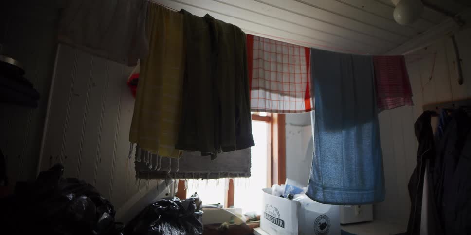 Colorful towels air dry on a clothesline strung across a cluttered room, backlit by a window
