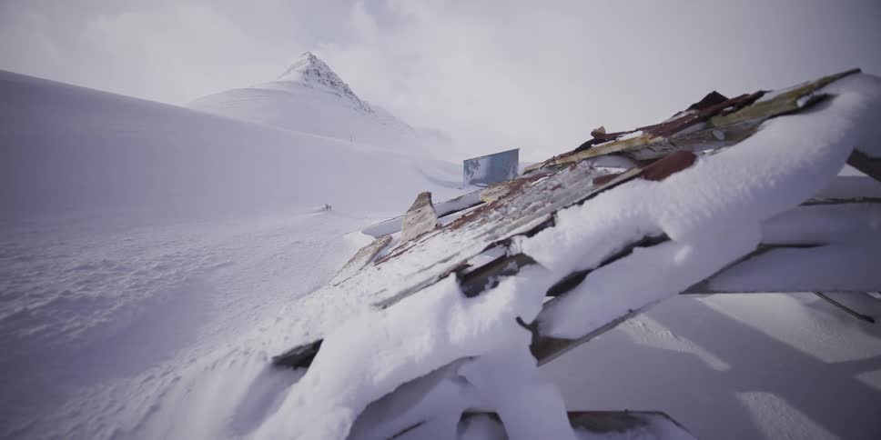 Slow dolly shot past a snow-covered collapsed roof reveals a desolate and frozen mountain landscape in the arctic