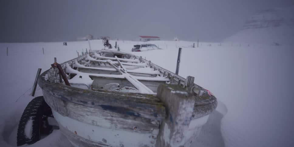 A slow pull-back reveals a weathered wooden boat abandoned in a vast, snowy landscape during a blizzard