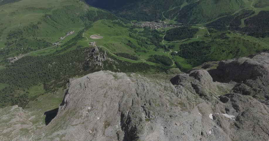 An aerial view from a rugged mountain summit looking down into a lush green valley with a small village nestled among the trees