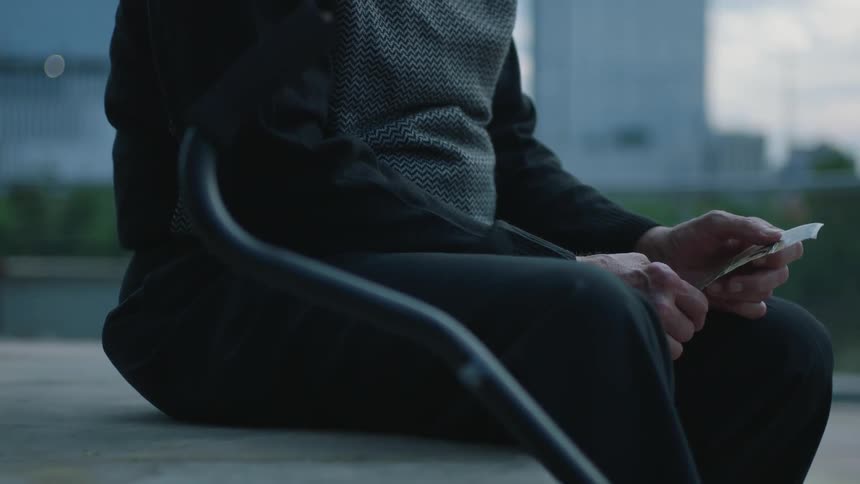 A man is sitting outside looking at a piece of paper