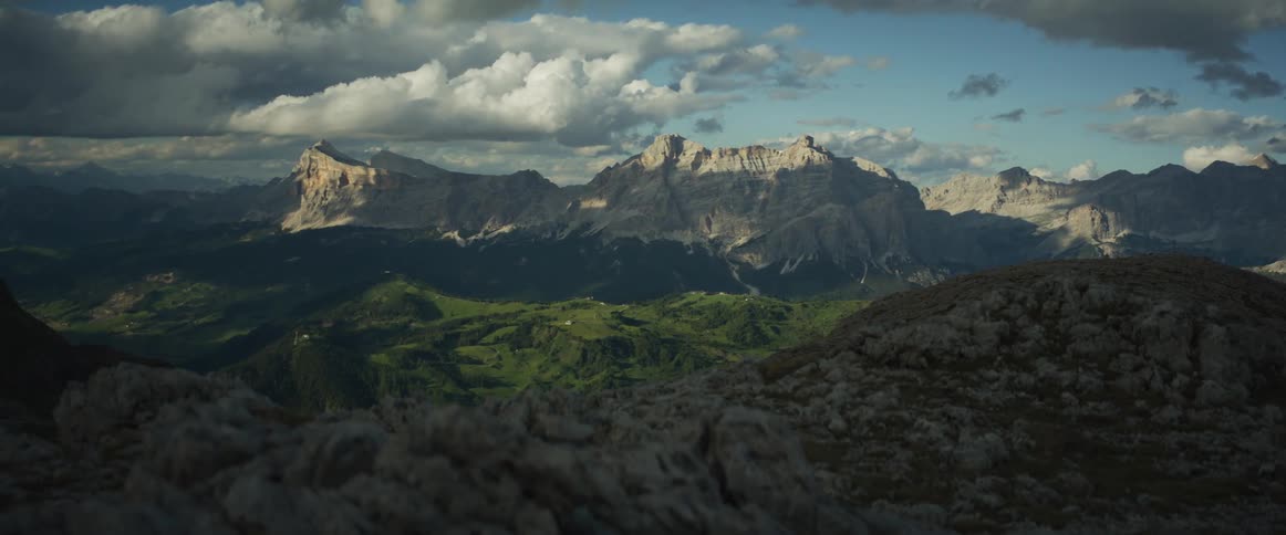 A slow slider shot reveals the majestic sunlit peaks of a mountain range towering over a verdant green valley