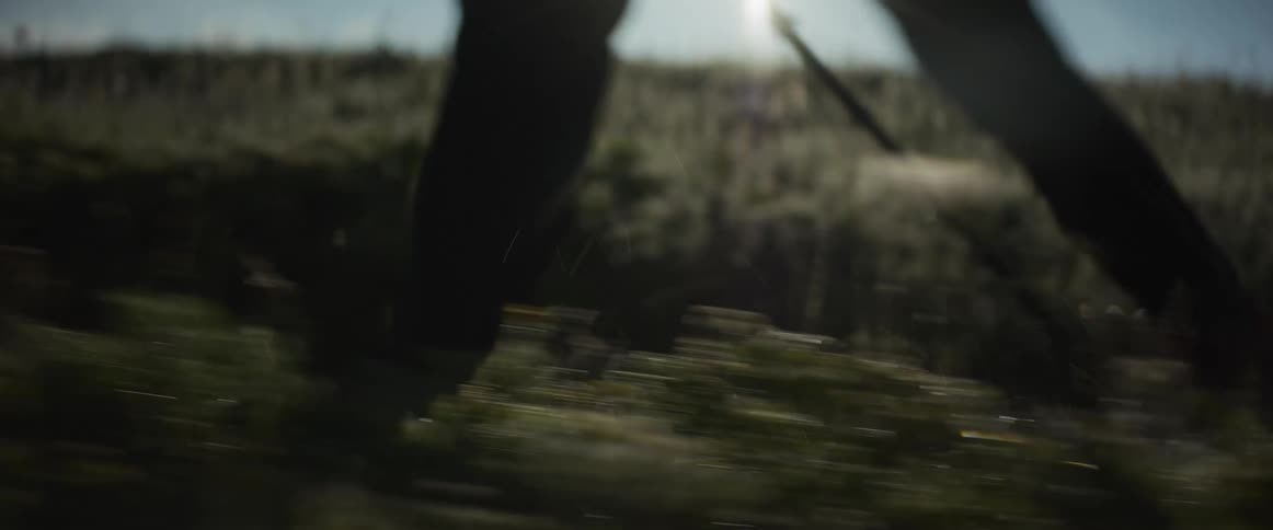 Dramatic low angle tracking shot of a silhouetted hiker's feet and legs moving quickly across a grassy field at sunrise