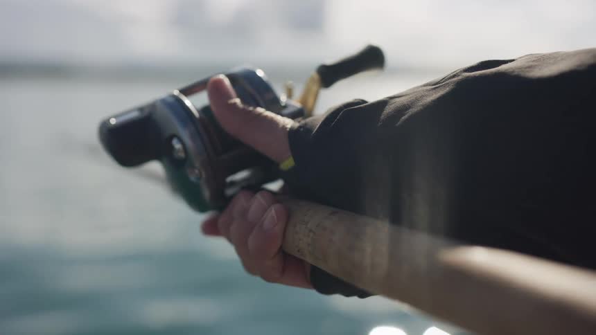 Slow motion close up of a fisherman's hand on a baitcasting reel while fishing over the water
