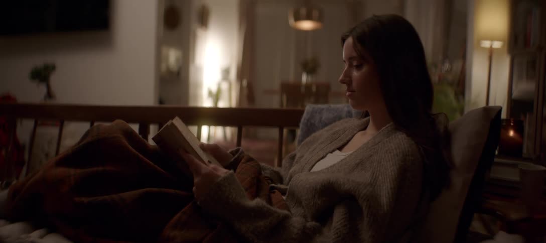 A woman enjoys a peaceful evening at home, reading a book while wrapped in a warm blanket on the couch