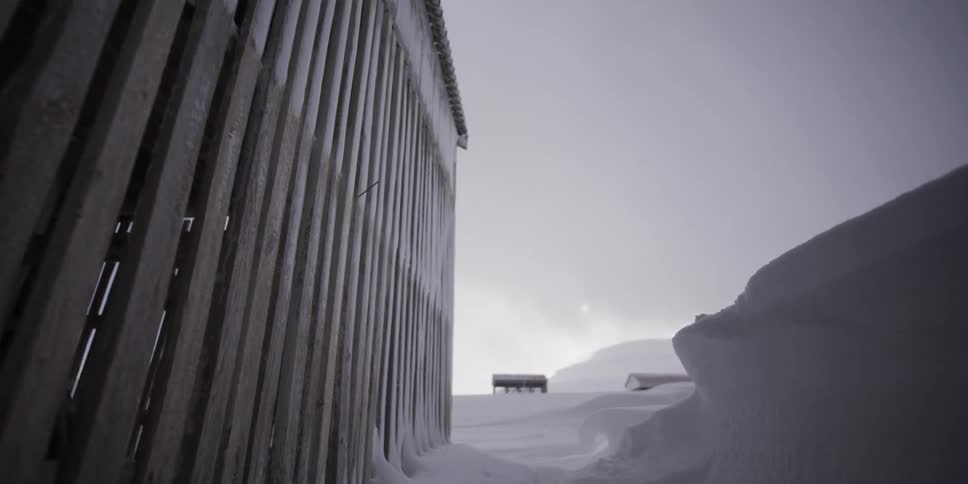Slow dolly-out from a traditional wooden fish drying rack in a vast, snow-covered arctic landscape