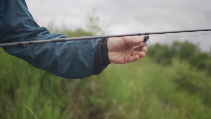 Slow motion close-up reveals a fly fisherman in waders inspecting the fly lure on their rod