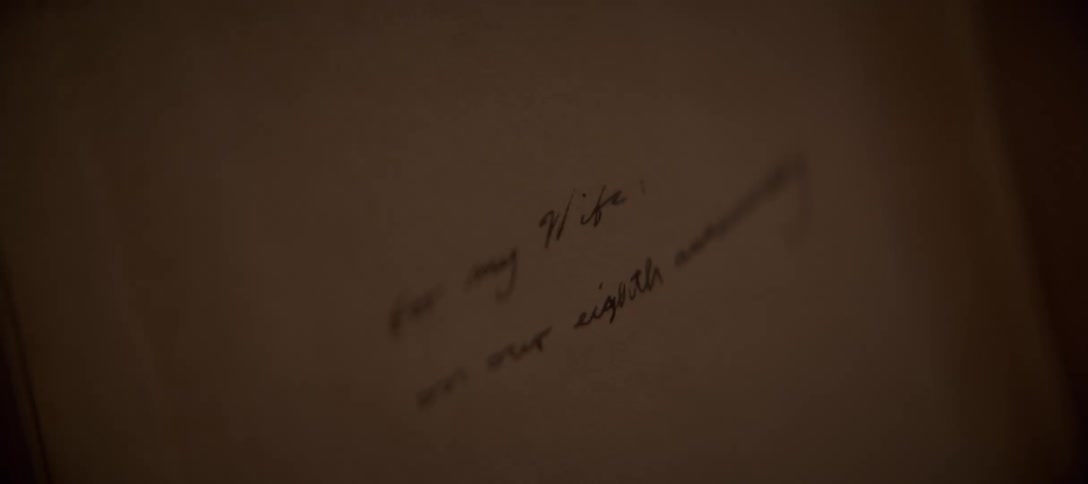 A close-up of a handwritten anniversary note to a wife on a piece of paper in a dimly lit room