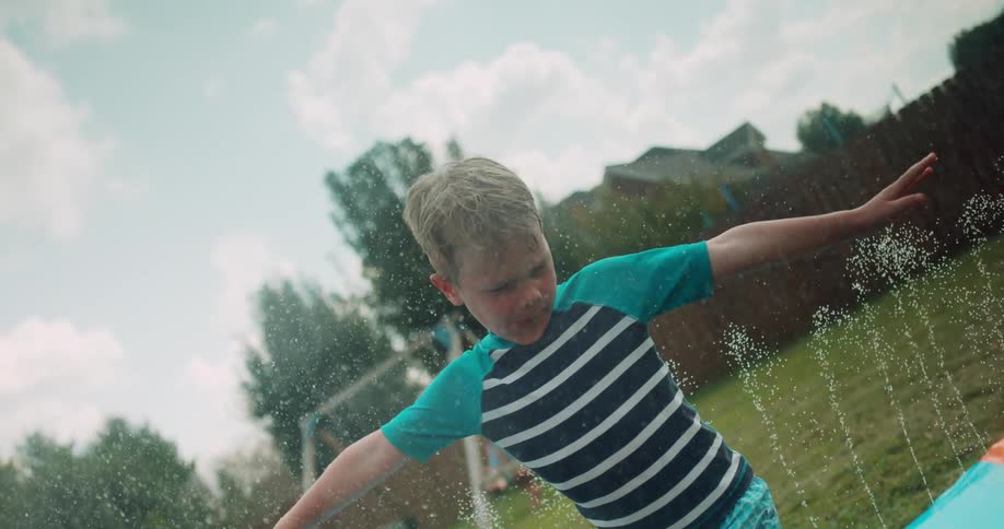 Little boy twirls around many sprinklers in backyard,