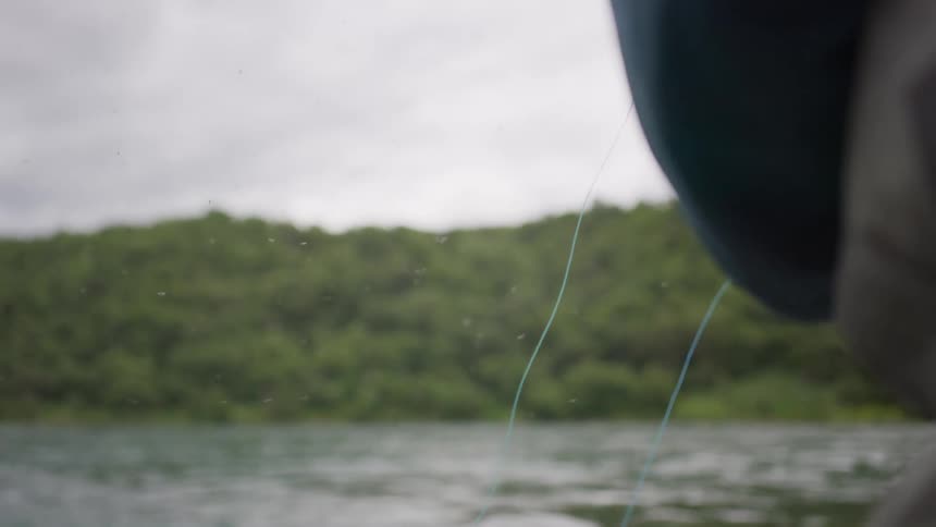 Slow motion close-up of a person's hands as they expertly cast and reel in a fly-fishing line on a calm river