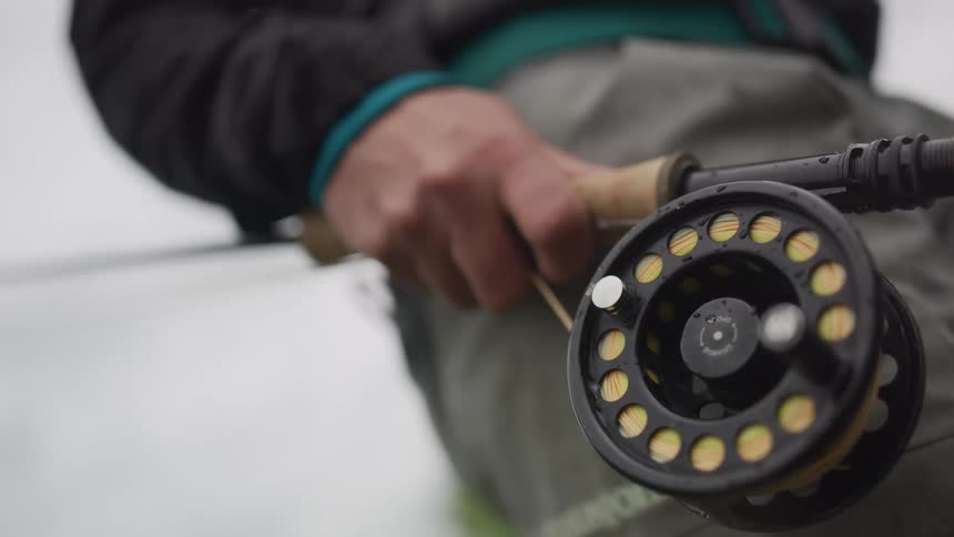 Close up slow motion rack focus from a fly fishing reel to a fisherman's hand gripping the rod