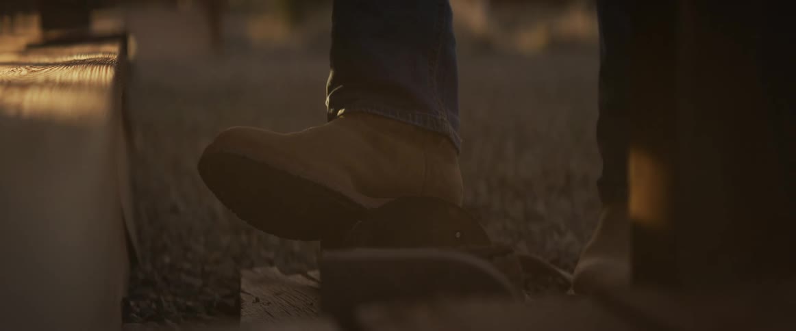 A cowboy's boot slowly lifts out of a saddle stirrup in the warm glow of sunset in slow motion