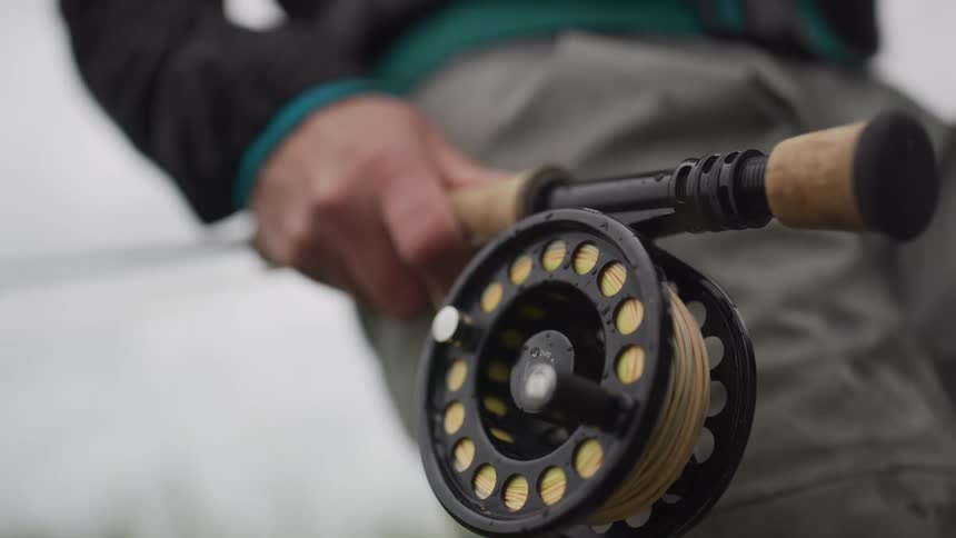 Slow-motion close-up of a fly fisherman's hand on a rod with a rack focus to the reel