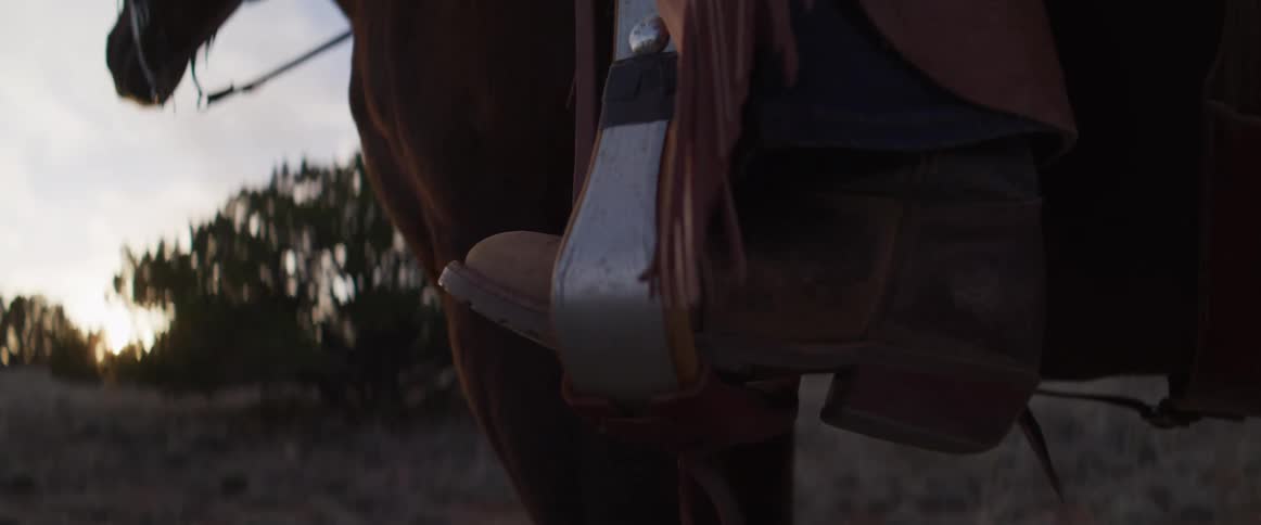 A close-up shot of a cowboy's boot in a stirrup while sitting on a horse at sunset