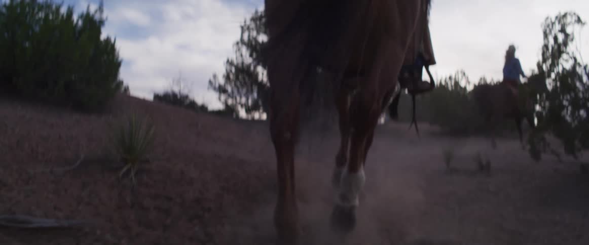 A dramatic slow-motion close-up captures the powerful legs of a horse galloping on a dusty trail at dusk