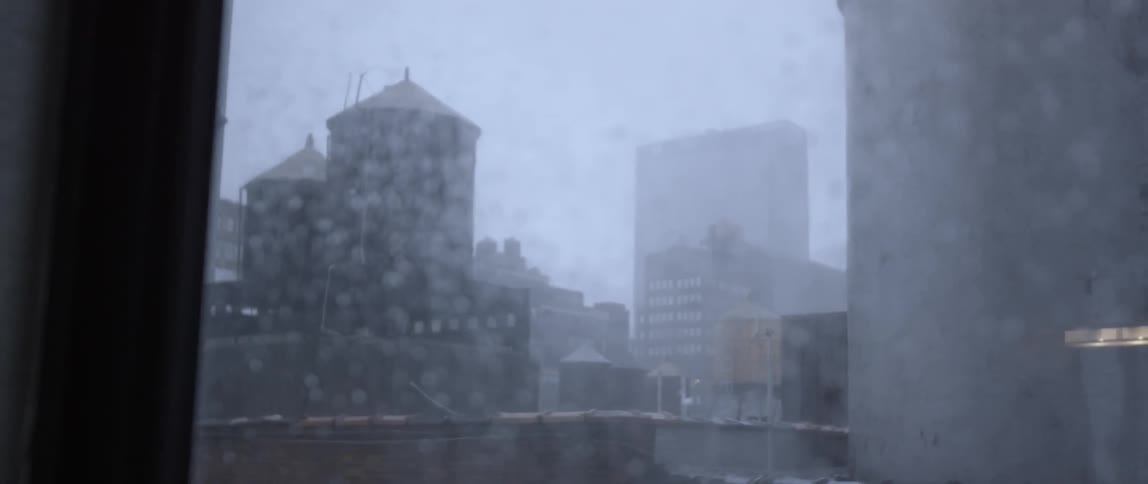 Rain falls on city buildings and on a window pane