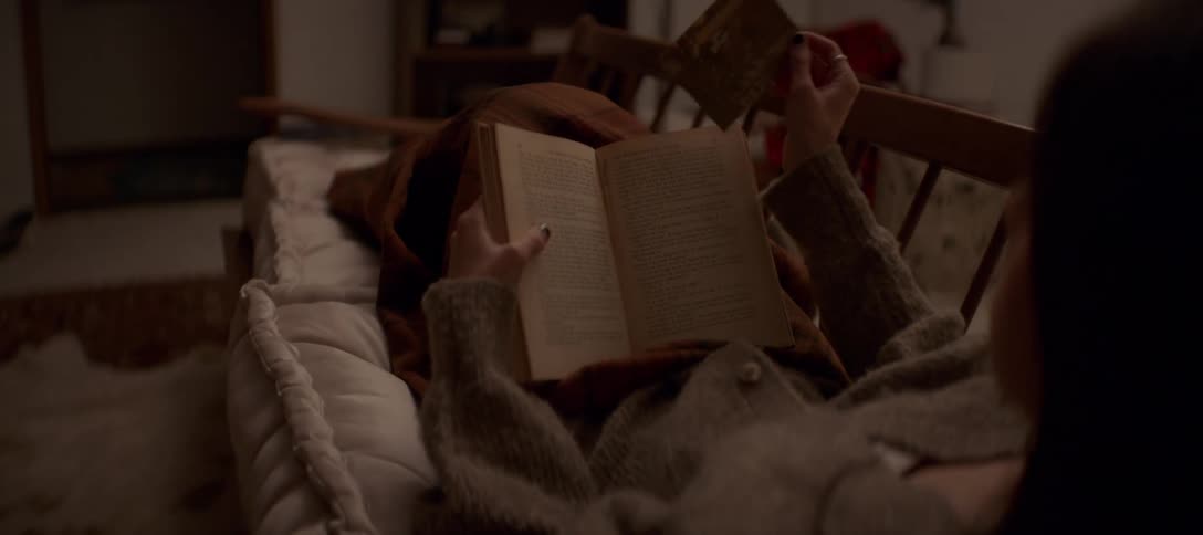 A woman relaxing on a couch reads a book and discovers an old photograph tucked inside the pages