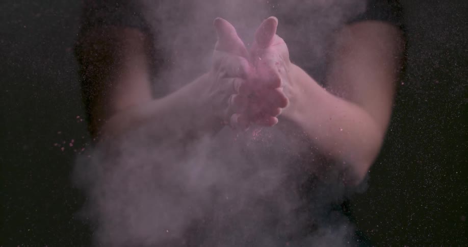 A woman claps her hands together with pink dirt