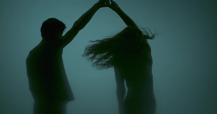 Man takes woman's hand and spins her around in foggy setting