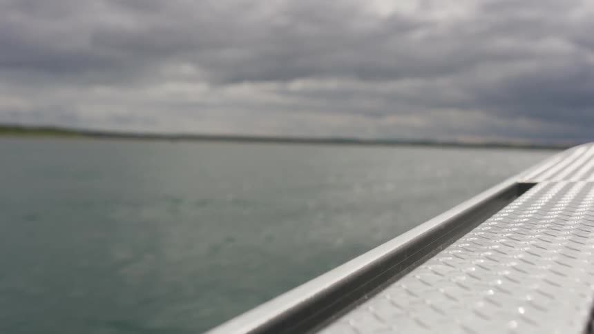 A serene, out-of-focus view from a metal boat floating on a large body of water under a cloudy sky