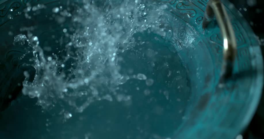 Water pours in splashes inside of the blue bowl