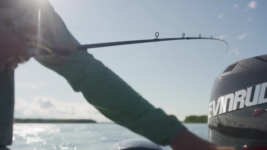 A fisherman holds a bent fishing rod while out on a boat on a calm, sunny day