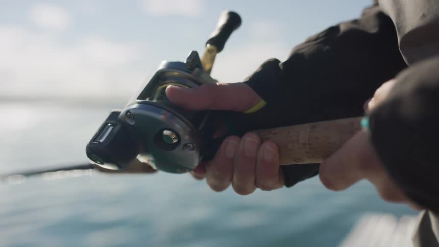 Close-up of a person's hands operating a fishing reel in slow motion while fishing on a boat in open water