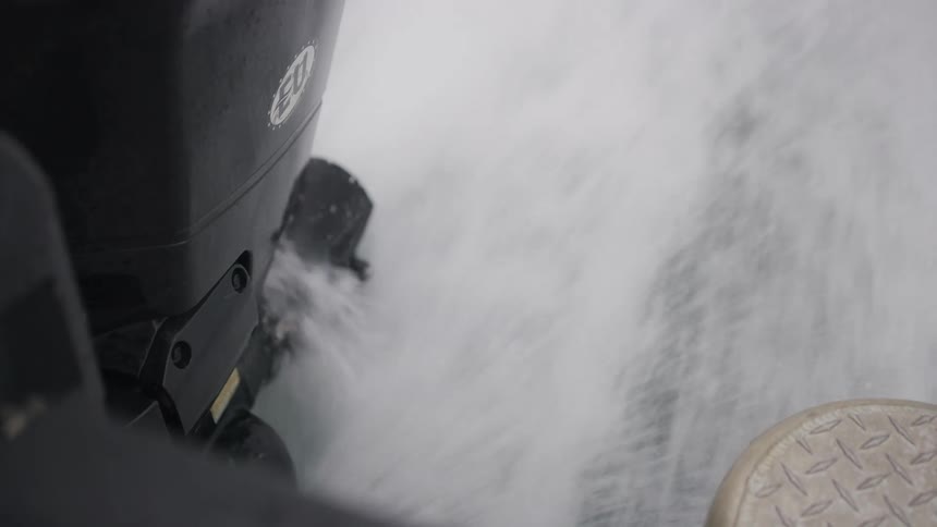 Slow motion close-up of a boat's outboard motor churning through the water and creating a frothy white wake