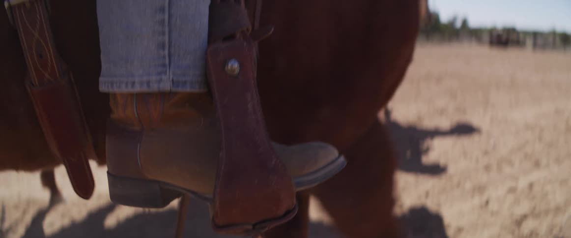 A close-up slow-motion shot of a cowboy boot in a stirrup as the rider's horse walks through a dusty pen