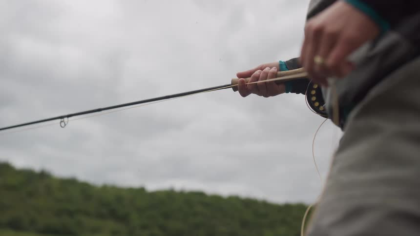 A close-up slow-motion shot of a fly fisherman casting their line on a cloudy day in nature