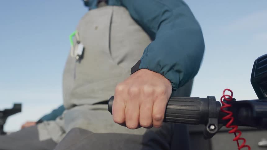 A close-up shot of a person's hand firmly gripping the tiller of an outboard motor while driving a boat