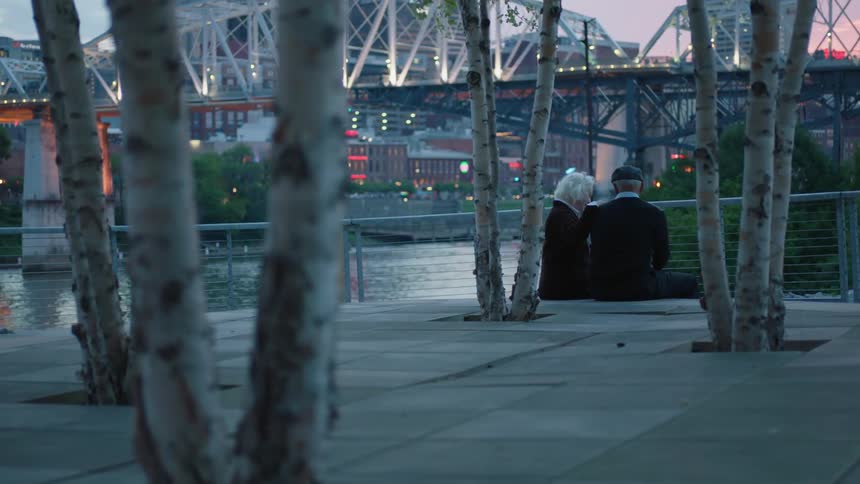 Two people sit by the water talking