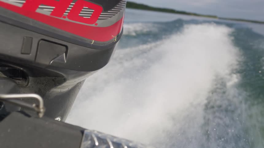A close-up slow-motion shot of a speedboat's outboard motor creating a powerful wake as it speeds across the water