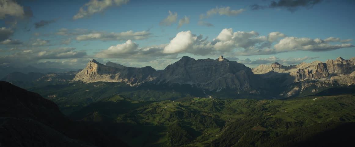 A stunning timelapse of clouds moving over a majestic mountain range, casting shifting shadows on the lush green valleys below