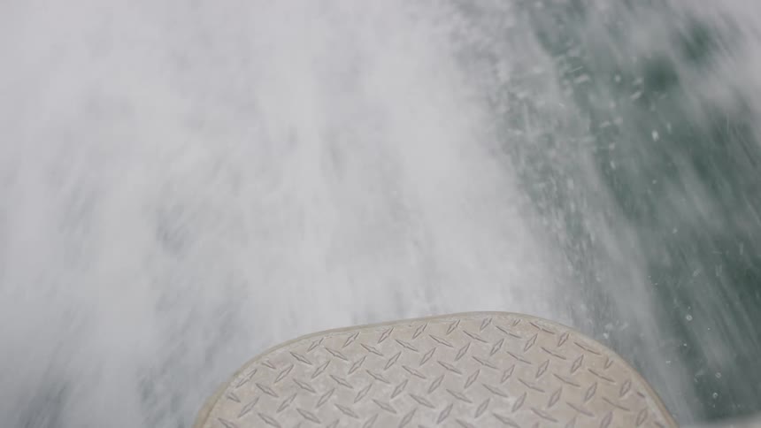 View from the deck of a speeding boat looking down at the splashing water and wake
