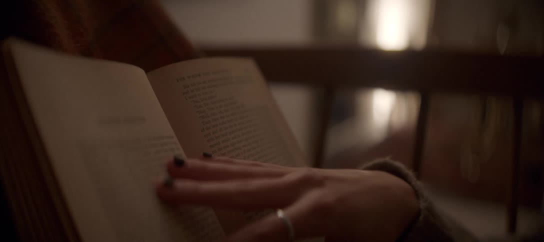 A person's hand with a ring turns the pages of an old book while relaxing in a cozy sweater