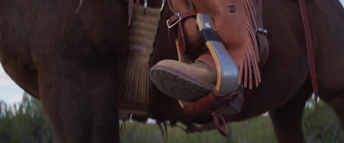 A close-up of a cowboy's boot resting in a stirrup while sitting atop a brown horse