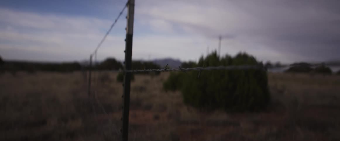 A slow focus pull along a desolate barbed wire fence with a tumbleweed caught in the wire in a dry field