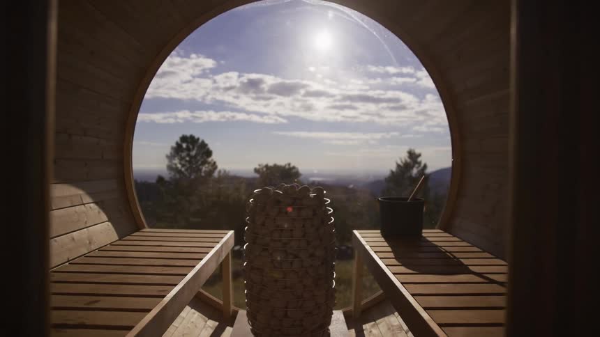 A slow push-in reveals the interior of a barrel sauna with a panoramic round window overlooking a sunny landscape