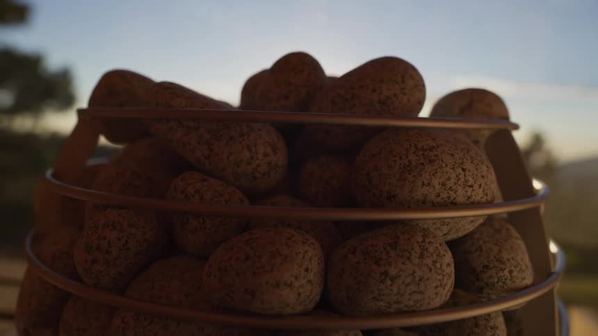 A slow push-in shot focuses on hot sauna stones as steam gently rises against a warm, sunlit background