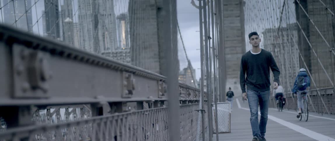 A young man is walking across a bridge in an urban setting