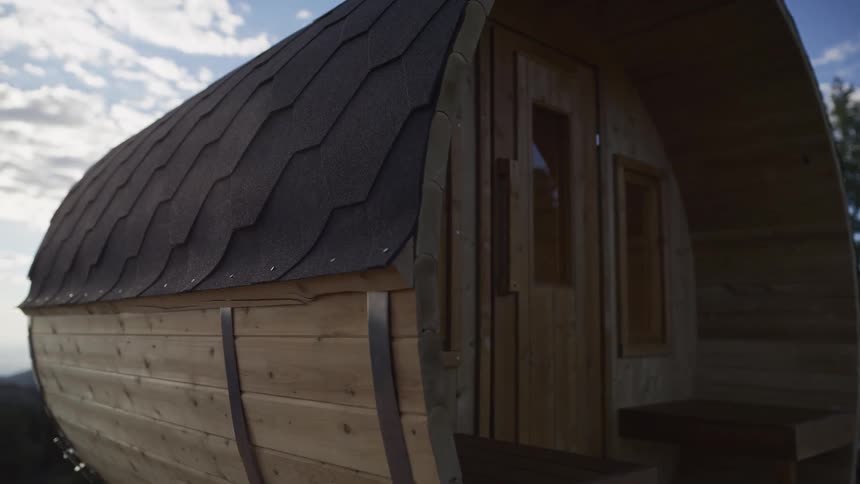 A slow pull-back shot reveals a rustic wooden barrel sauna in a peaceful outdoor setting under a partly cloudy sky