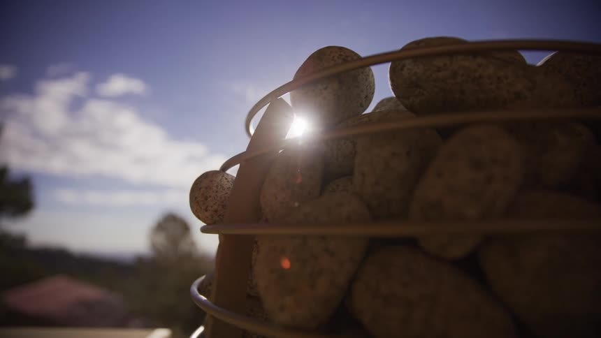 A close-up slow dolly shot reveals a bright sun flare behind sauna stones on a beautiful day