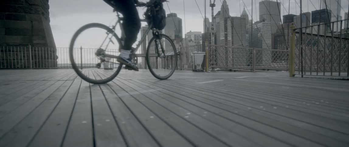 The boardwalk is near a city as a person rides their bicycle